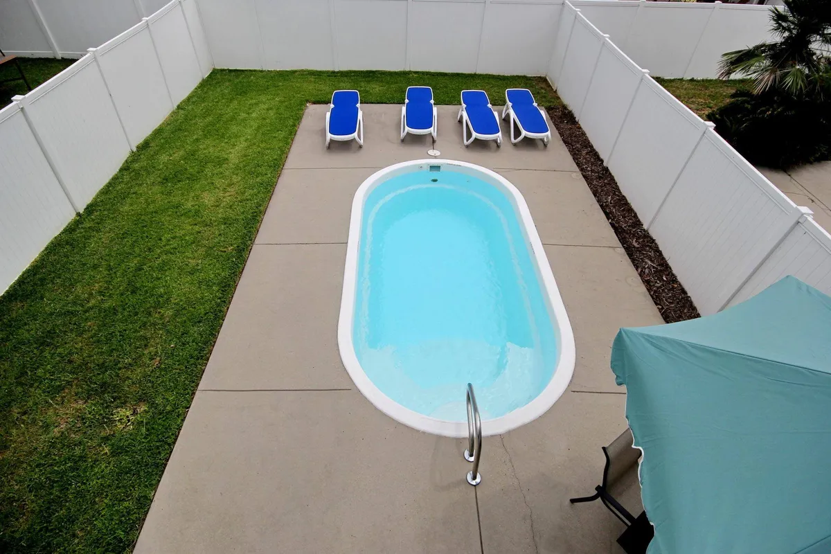 This image captures the inviting exterior swimming pool area with lounge chairs arranged for both sunbathing and social gatherings. The tranquil ambiance of the yard is accentuated by the soft natural light, suggesting an ideal spot for relaxation or lighthearted poolside activities.