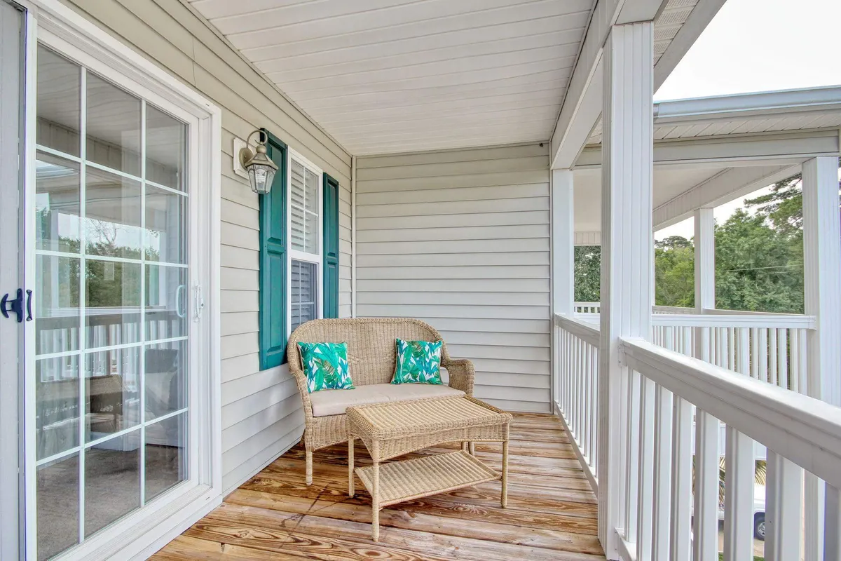 A sunlit porch scene with wicker seating, decorative cushions, and a wooden deck, offering tranquil views and a relaxed atmosphere. The high-top table is perfectly positioned for breezy breakfasts or sunset cocktails overlooking the ocean.