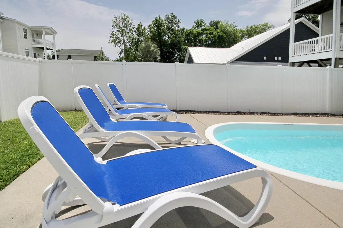 An exterior scene showing a tranquil pool surrounded by lounge chairs, a secure fence, and lush green grass. The setting is ideal for leisure, with ample space for families to relax together after a meal or to host casual outdoor feasts and picnics in a serene environment.