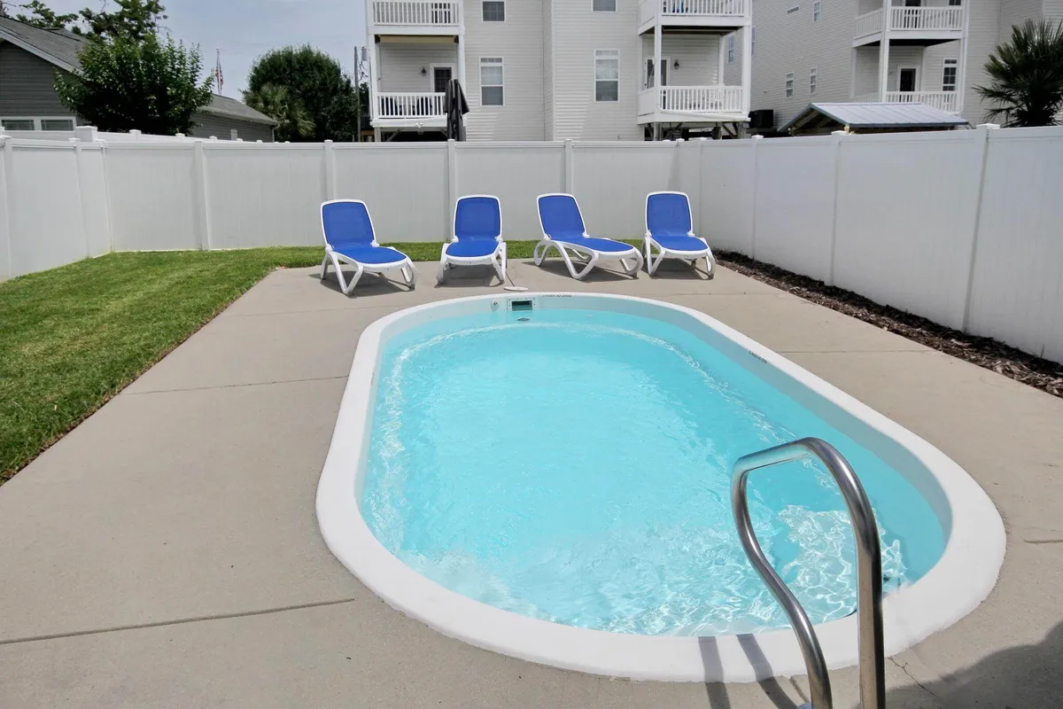 A vibrant exterior scene featuring a fenced swimming pool, several lounge chairs, and open space for outdoor games or gatherings. The setup hints at leisurely afternoons, family BBQs, and moments of togetherness under the sun.