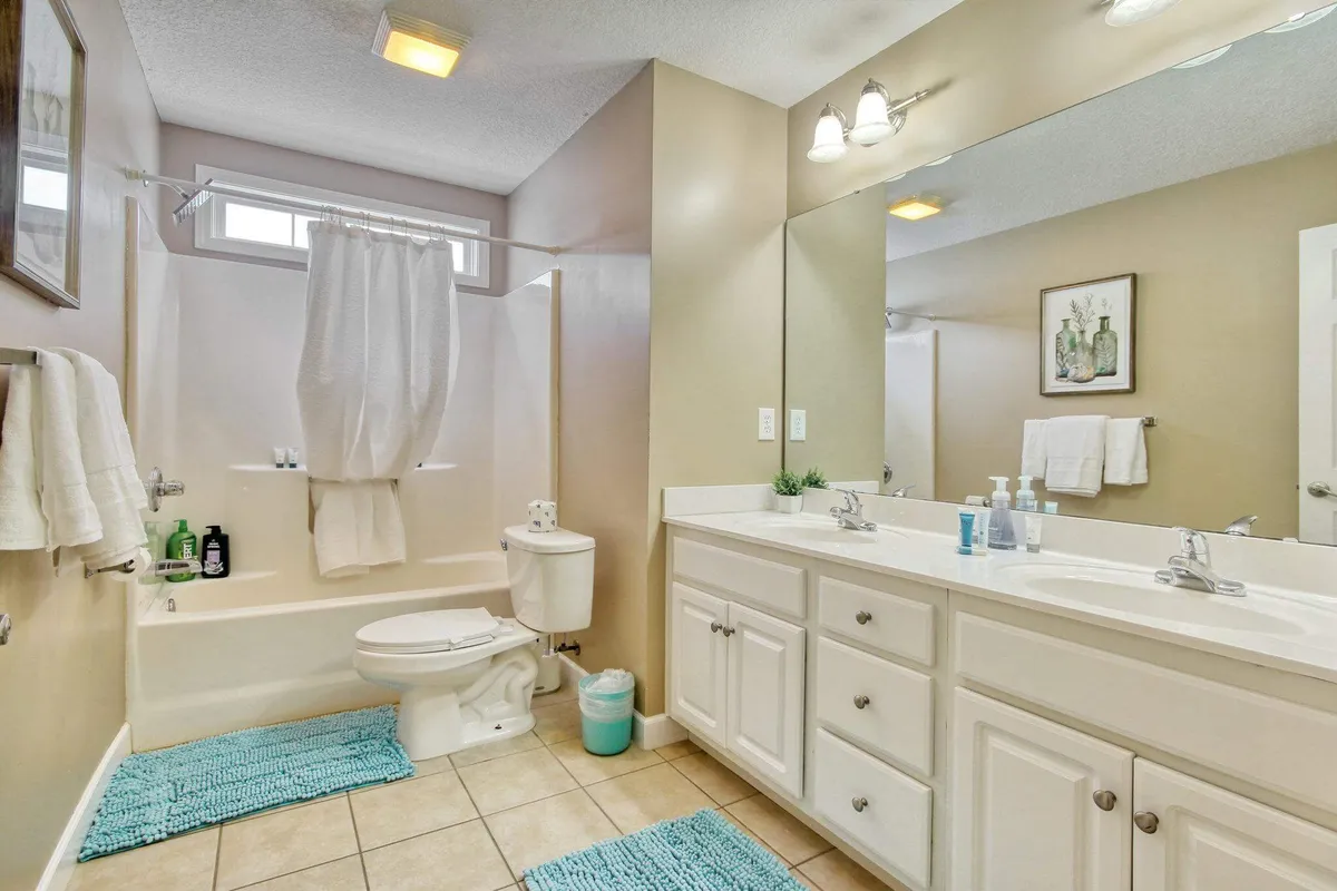 A spacious bathroom with a double sink vanity, large mirror, bathtub with a shower curtain, and decorative artwork. The space feels inviting and functional, ideal for both quick morning routines and relaxing evening baths.