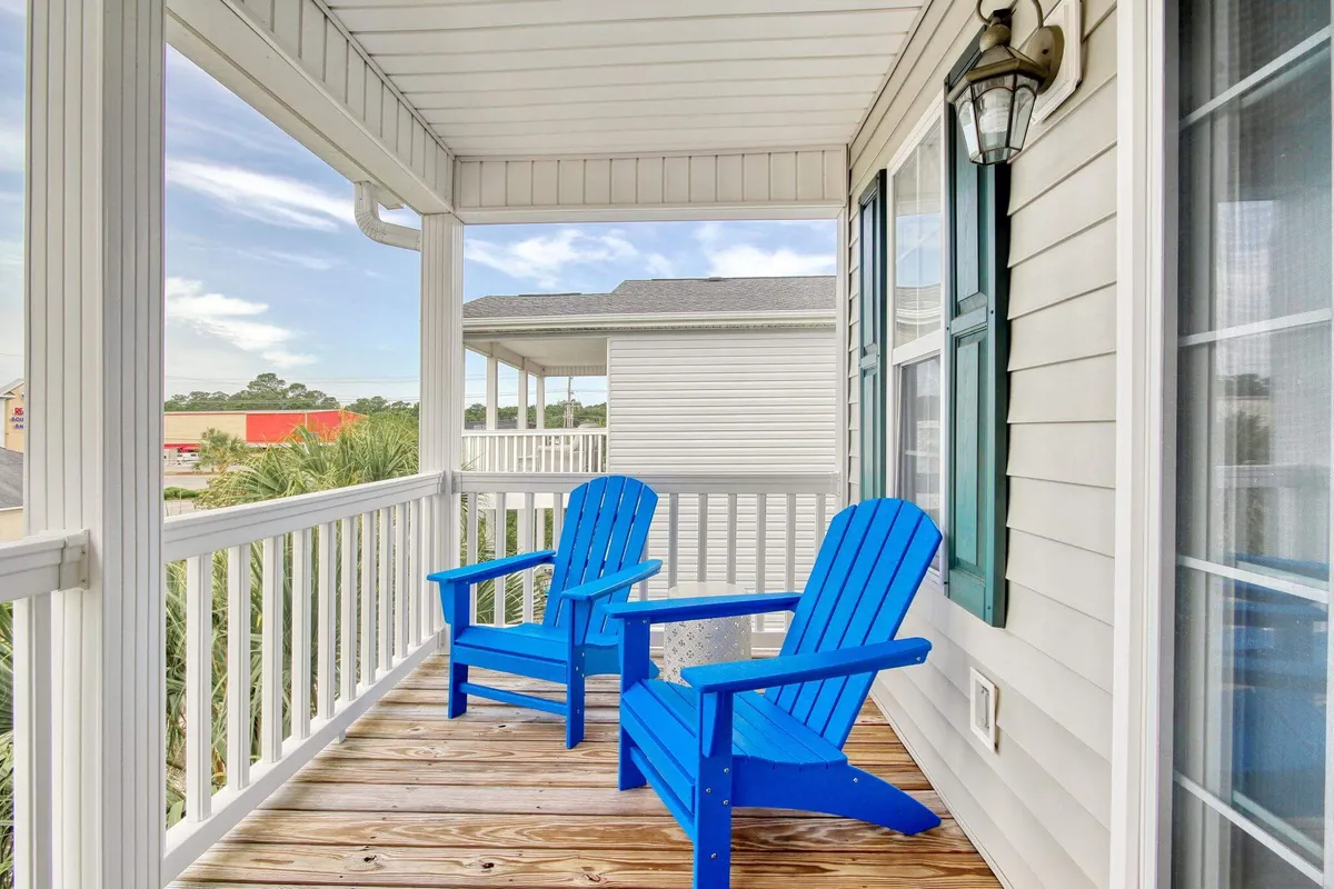 A tranquil exterior deck featuring blue Adirondack chairs and a white railing, perfect for lounging while enjoying morning coffee, reading, or watching sunsets. The wooden deck hints at a relaxed, open-air environment ideal for embracing the coastal lifestyle.