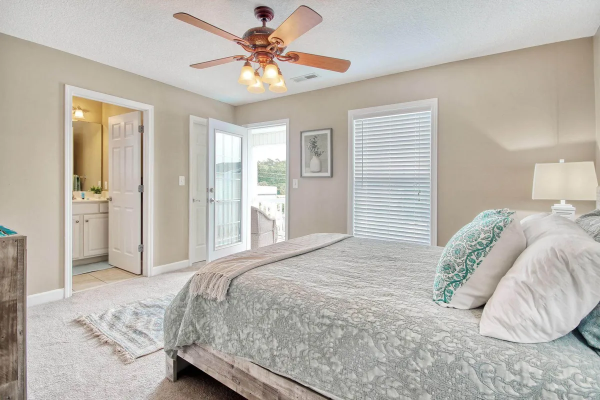 A cozy, sunlit bedroom featuring balcony doors that open to an outdoor space. With a comfortable bed, ceiling fan, and an inviting atmosphere, the image captures both the restful retreat inside and the potential to step out and explore the local scene.