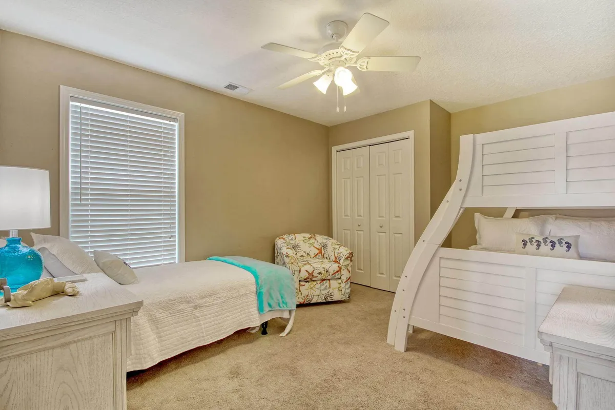 A comfortable family-friendly bedroom with a bunk bed and a single bed, complemented by a colorful chair and a cozy table lamp. The decor suggests a playful, relaxed atmosphere ideal for kids or groups.