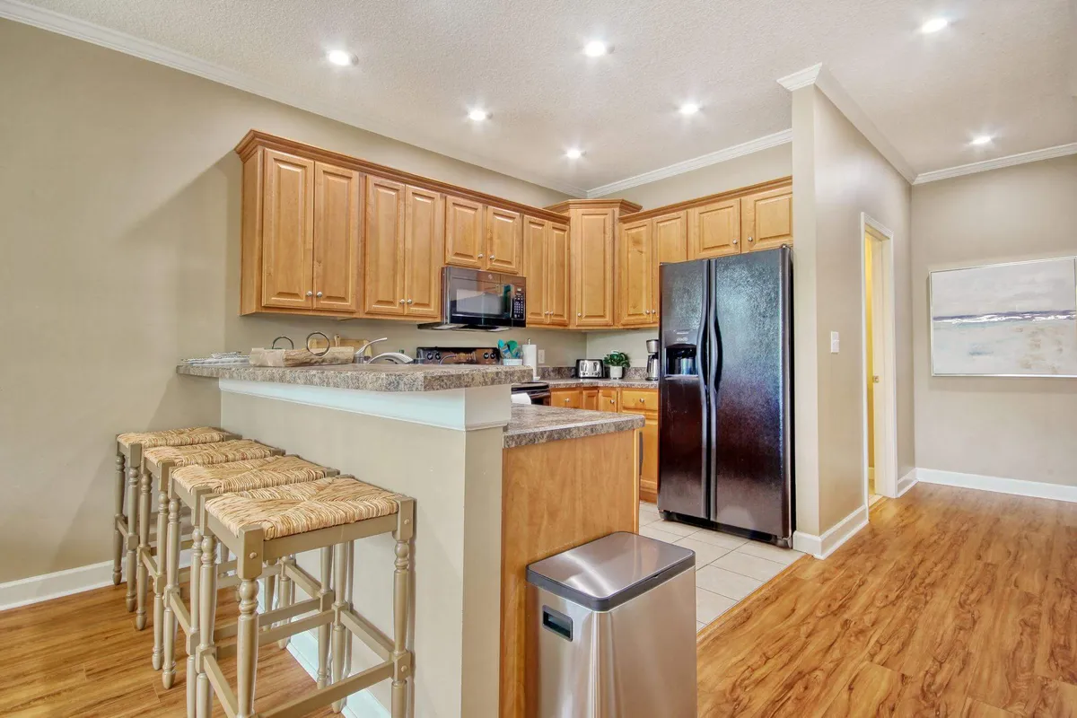 An airy interior kitchen featuring warm wooden cabinetry, a granite countertop with bar stools, and soft natural light. The space is designed for cooking and entertaining, with ample room for family and friends to gather and prepare meals together.